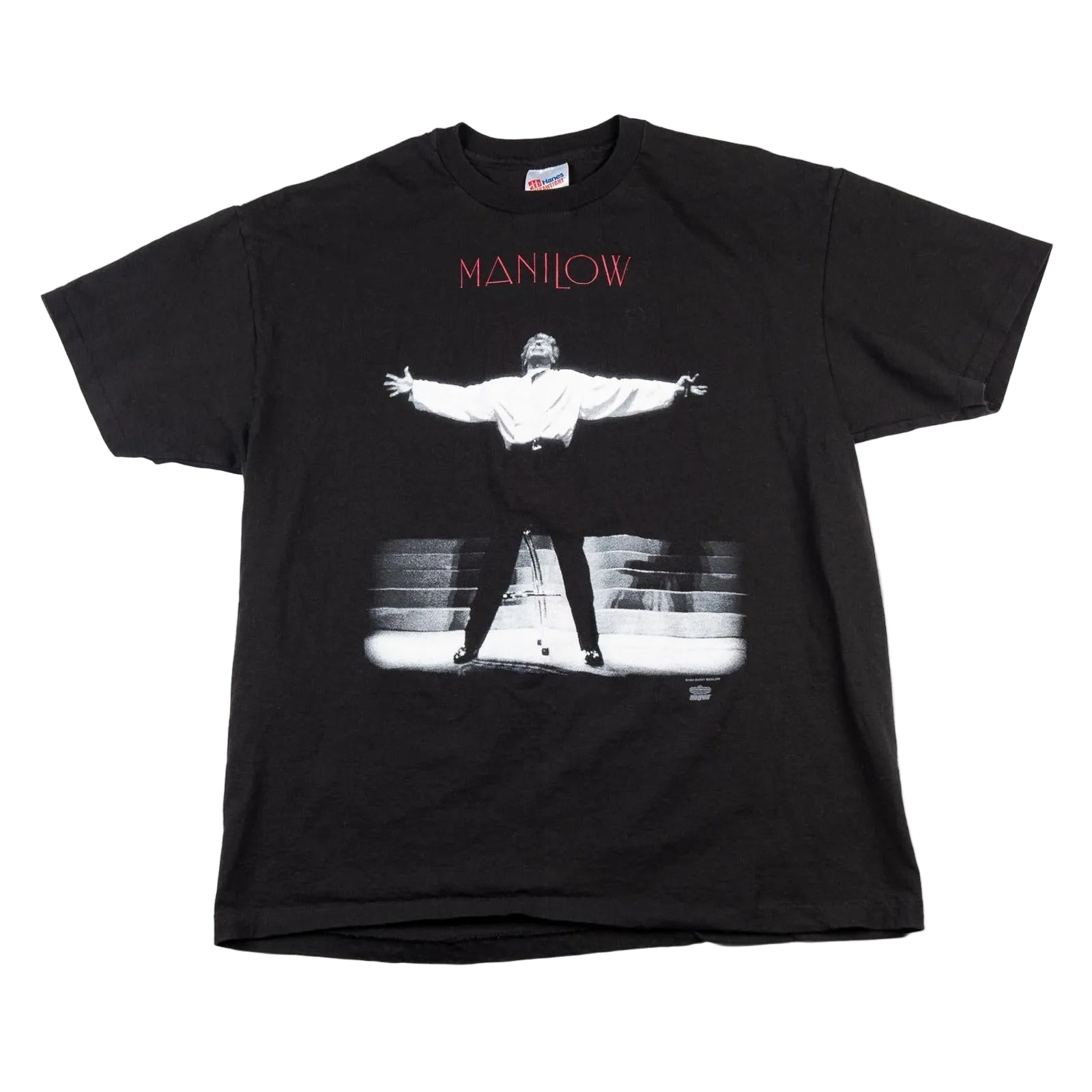 Black t-shirt with a graphic of a person on stage and 'Manilow' text, on a white background